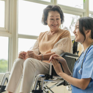 asian young caregiver caring for her elderly patient at senior daycare Handicap patient in a wheelchair at the hospital talking to a friendly nurse and looking cheerful nurse wheeling Senior patient